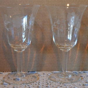 May include: Two clear glass wine glasses with etched floral designs. The glasses have a tall, slender stem and a wide, round bowl.