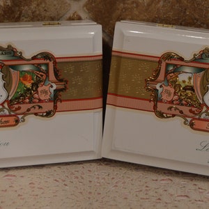 Op de afbeelding: Twee witte houten dozen met gouden en roze versieringen. De dozen hebben een label met de tekst "My Father Cigars" en "La Riqueza 1993".