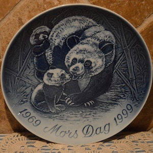 Könnte beinhalten: Blaue und weiße Porzellanplatte mit einem Reliefbild von zwei Pandas, einem Erwachsenen und einem Jungtier, in einem Bambuswald. Die Platte trägt den Text "1969 Mors Dag 1999" am unteren Rand.