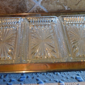 Puede incluir: Una bandeja de servir plateada con tres platos de vidrio transparente. Los platos tienen un patrón de estrella y son perfectos para servir aperitivos o aperitivos.