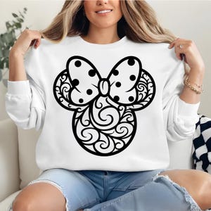 May include: White sweatshirt featuring a black Minnie Mouse design. The design includes a polka-dot bow and decorative swirls. The sweatshirt is long-sleeved and made of a soft material.