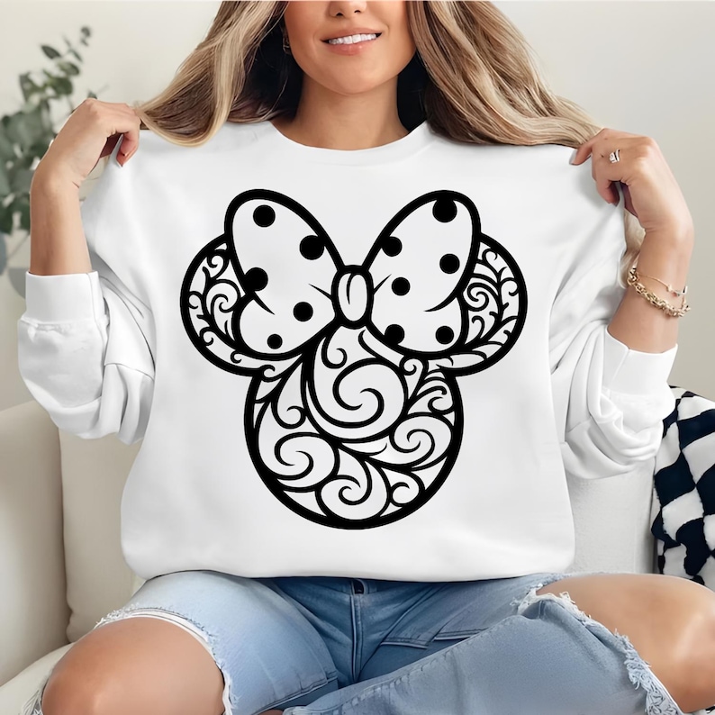 May include: White sweatshirt featuring a black Minnie Mouse design. The design includes a polka-dot bow and decorative swirls. The sweatshirt is long-sleeved and made of a soft material.