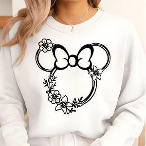 May include: White sweatshirt featuring a black floral Minnie Mouse design. The design includes a bow, ears, and floral accents. The sweatshirt is a crew neck style.