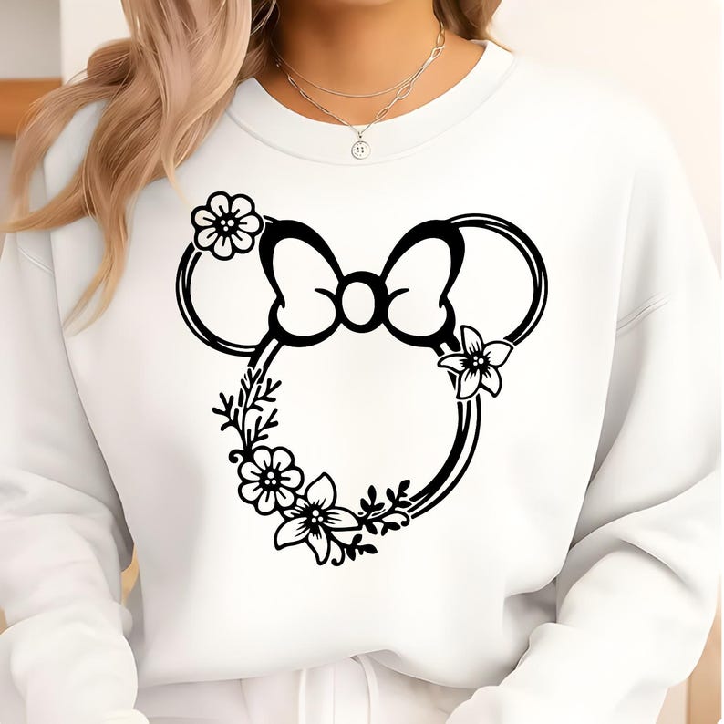 May include: White sweatshirt featuring a black floral Minnie Mouse design. The design includes a bow, ears, and floral accents. The sweatshirt is a crew neck style.