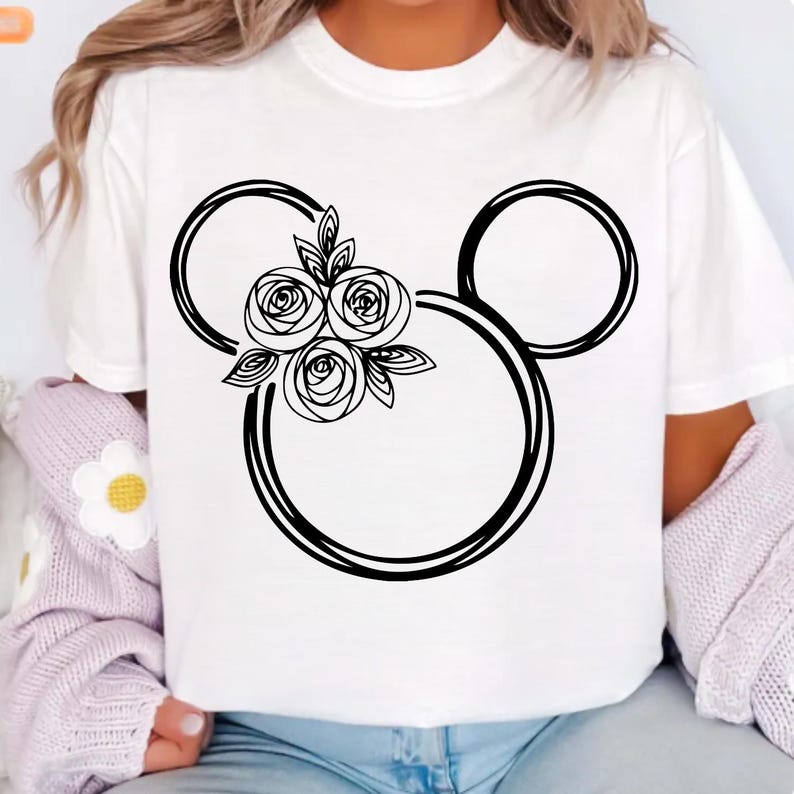 May include: White t-shirt featuring a black floral Mickey Mouse design. The design includes three roses and leaves within the iconic mouse silhouette. The shirt is a casual, everyday wear item.