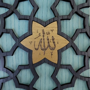 May include: Intricate wooden panel with a geometric star pattern in black and gold. The central star displays Arabic calligraphy on a gold background, set against a light blue backdrop. The design is detailed and ornate.