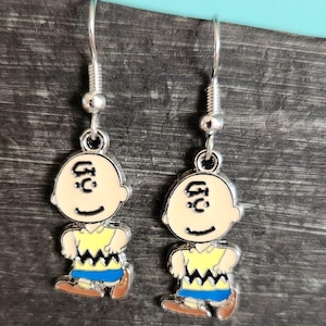 Può includere: Un paio di orecchini pendenti color argento con un design a personaggio dei cartoni animati. Ogni orecchino presenta un personaggio sorridente con un viso beige, camicia gialla, pantaloncini blu e scarpe marroni. Chiusura a gancio semplice.