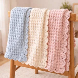 May include: Three crocheted blankets in pastel colors draped over a wooden chair. The blankets are light blue, cream, and pink, each with a scalloped edge. The blankets have a textured, woven appearance.