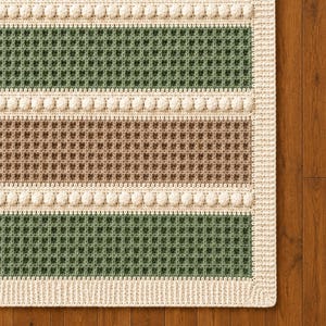 May include: A rectangular crochet blanket featuring alternating horizontal stripes of sage green and light brown in a waffle stitch pattern. The stripes are separated by rows of cream-coloured bobble stitches, with a solid cream-coloured border.