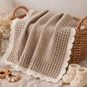 Può includere: Una coperta all'uncinetto beige con un centro a punto waffle e un bordo smerlato color crema, drappeggiata su un cesto di vimini intrecciato. La coperta è accompagnata da un paio di scarpine per neonati all'uncinetto color crema e un anello in legno.