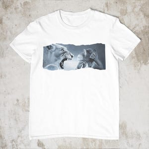 May include: White t-shirt featuring a graphic of a roaring lioness facing a contemplative chimpanzee. The artwork is in shades of gray and blue, set against a torn paper effect. The shirt is a classic crew neck style.