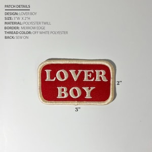 May include: A rectangular sew-on patch with a red background and off-white border featuring the text LOVER BOY in off-white thread. The patch measures 3 inches wide by 2 inches high. Text details include design, size, material, border, and thread color.