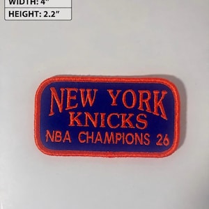 May include: A rectangular embroidered patch with a blue background and orange border. The text reads NEW YORK KNICKS NBA CHAMPIONS 26 in orange lettering. The patch measures 4 inches in width and 2.2 inches in height as indicated in the image.
