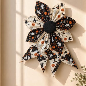 Puede incluir: Un tapiz de tela con forma de flor grande de pétalos puntiagudos. La tela presenta un estampado de Halloween con gatos negros, fantasmas blancos, calabazas naranjas, sombreros de bruja y telarañas sobre fondos negros y crema, con un centro negro.