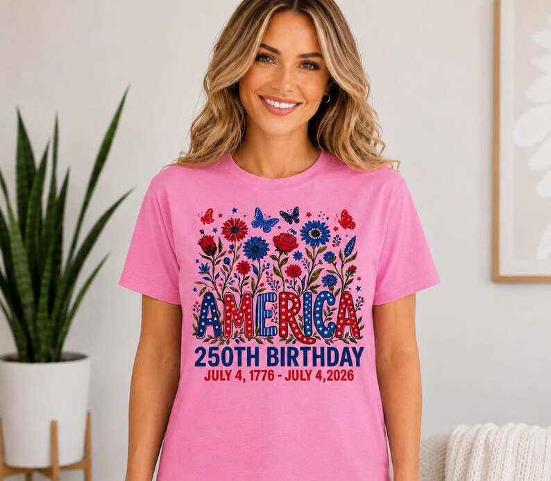 May include: A pink short-sleeved t-shirt featuring a graphic of red, white, and blue flowers and butterflies. The text reads AMERICA 250TH BIRTHDAY JULY 4, 1776 - JULY 4, 2026. The design uses a patriotic colour palette with stars and polka dot patterns.