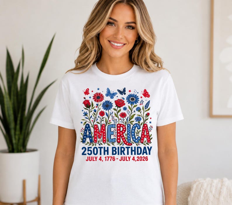 May include: A white short-sleeve t-shirt featuring a graphic of red and blue flowers, butterflies, and the text AMERICA 250TH BIRTHDAY JULY 4, 1776 - JULY 4, 2026. The design uses a patriotic colour palette with stars and polka dot patterns.