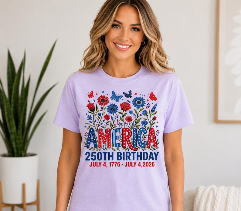 May include: A light purple t-shirt featuring a graphic of red and blue flowers and butterflies. The text reads AMERICA 250TH BIRTHDAY JULY 4, 1776 - JULY 4, 2026. The word AMERICA is styled in red, white, and blue patterns with stars and dots.