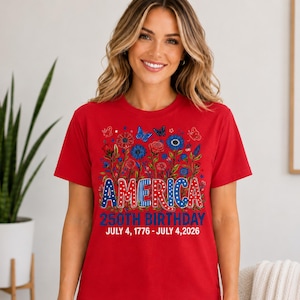 May include: A red short-sleeved t-shirt featuring a graphic of blue and red flowers, butterflies, and the text AMERICA 250TH BIRTHDAY JULY 4, 1776 - JULY 4, 2026. The word AMERICA is styled with stars and stripes patterns in red, white, and blue.