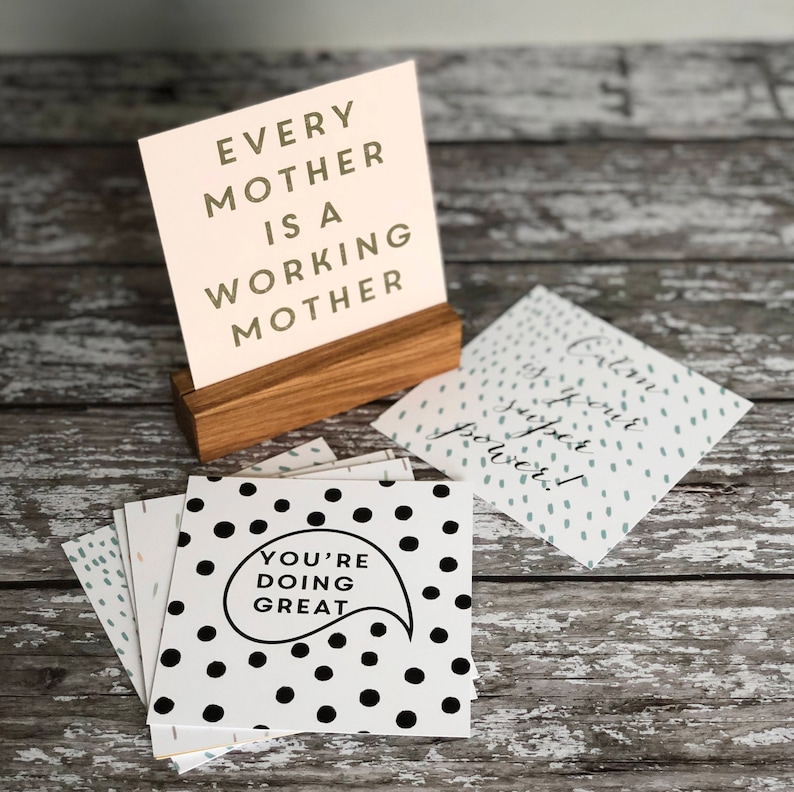 Op de afbeelding: Een verzameling wenskaarten met inspirerende boodschappen. E&eacute;n kaart toont "Every Mother Is A Working Mother" in een houten houder. Andere kaarten hebben stippen en de zinnen "You're Doing Great" en "Calm is your super power!"