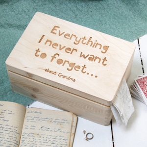 May include: A wooden box with a lid that has the words "Everything I never want to forget... about Grandma" engraved on it. The box is sitting on a white surface.