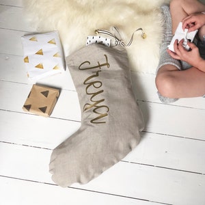 May include: A beige linen Christmas stocking with the name "Freya" written in gold lettering.