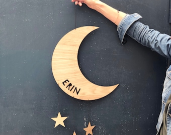 May include: Wooden crescent moon with the name "Erin" engraved on it. The moon is hanging from a string with three small wooden stars attached.