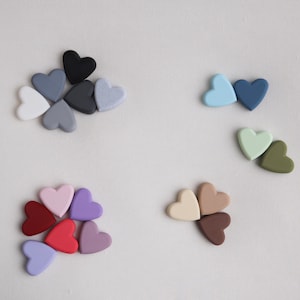 May include: A collection of small heart-shaped beads in various colors, including white, shades of gray, black, light blue, dark blue, pale green, olive green, light pink, purple, dark red, bright red, cream, tan, and dark brown.