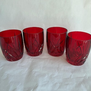 May include: Four ruby red drinking glasses. Each glass has a cylindrical shape with a textured, geometric design. The glasses are made of a transparent material, allowing light to pass through and highlight the intricate patterns. The glasses are suitable for serving beverages.