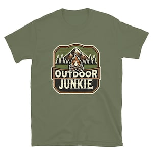Puede incluir: Una camiseta verde de manga corta con un logotipo de estilo vintage que presenta una cordillera, una fogata y el texto "Outdoor Junkie".