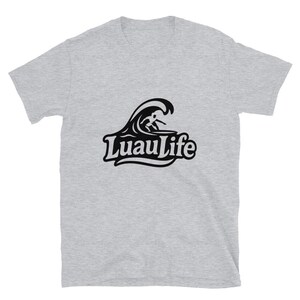 May include: A pale grey t-shirt with a black graphic of a surfer on a wave, and the words "Luau Life" in a decorative font. The shirt is made of a soft material and has short sleeves.