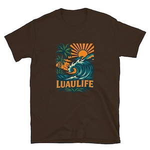 May include: Brown t-shirt featuring a vibrant graphic with a tropical theme. The design includes a stylized wave, sun, and palm trees, with the text "LUAULIFE" in a bold font. The artwork is in shades of blue, orange, and green.