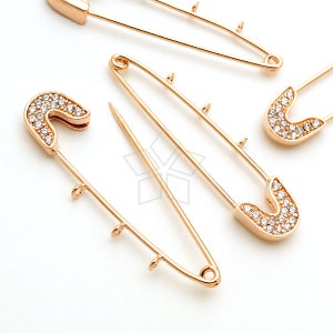 May include: Three gold safety pins with clear rhinestones. The pins are all closed and have a shiny finish.