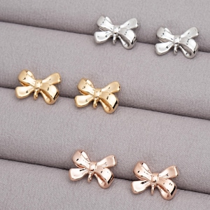 May include: A set of six bow-shaped earrings in three different colors: gold, silver, and rose gold. The earrings are small and delicate, and they would make a great gift for a friend or loved one.