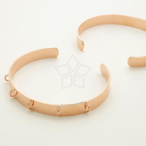 Puede incluir: Dos pulseras de metal de color oro rosa con anillas de salto. Las pulseras están abiertas y tienen un acabado liso y pulido.