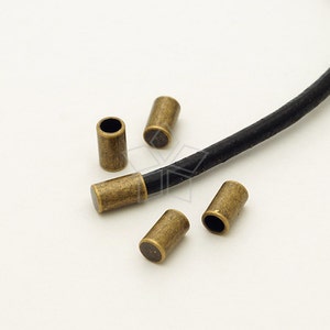 May include: Five antique gold-toned metal cord end caps for leather cord. The cord end caps are cylindrical with a small hole in the center.