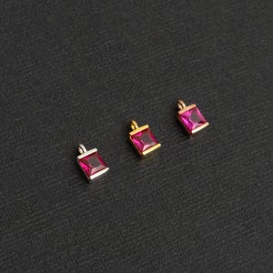 Può includere: Quattro ciondoli quadrati con una pietra preziosa rosa al centro. I ciondoli sono realizzati in diversi metalli: argento, oro e oro rosa.