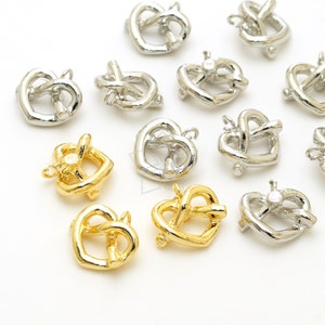 Op de afbeelding: Close-up van meerdere pretzel-vormige bedels in goud- en zilverkleuren. De bedels hebben een lus aan de bovenkant om aan sieraden te bevestigen. De pretzels zijn klein en gedetailleerd, met een klassiek pretzel-ontwerp.