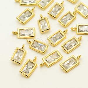 May include: A group of gold-toned rectangular charms with clear crystal accents. The charms have a loop at the top for attaching to jewelry.