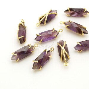 May include: A group of eight amethyst gemstone pendants with gold-toned metal settings. The pendants are shaped like long, pointed crystals and have a purple hue.