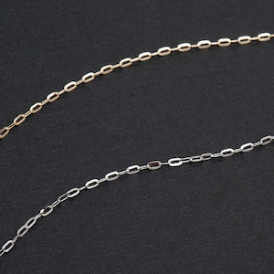 May include: Close-up of two delicate chain necklaces. One is gold-toned, the other is silver-toned. The chains are composed of small, elongated oval links. The background is a solid, dark grey colour.