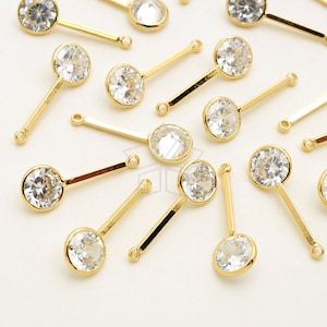 May include: A collection of gold-toned metal charms with clear round rhinestones. Each charm features a long, thin bar with a loop at the top and a round rhinestone at the bottom.