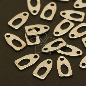 May include: A group of silver-toned metal oval-shaped charms with two holes each. The charms are scattered on a black surface.
