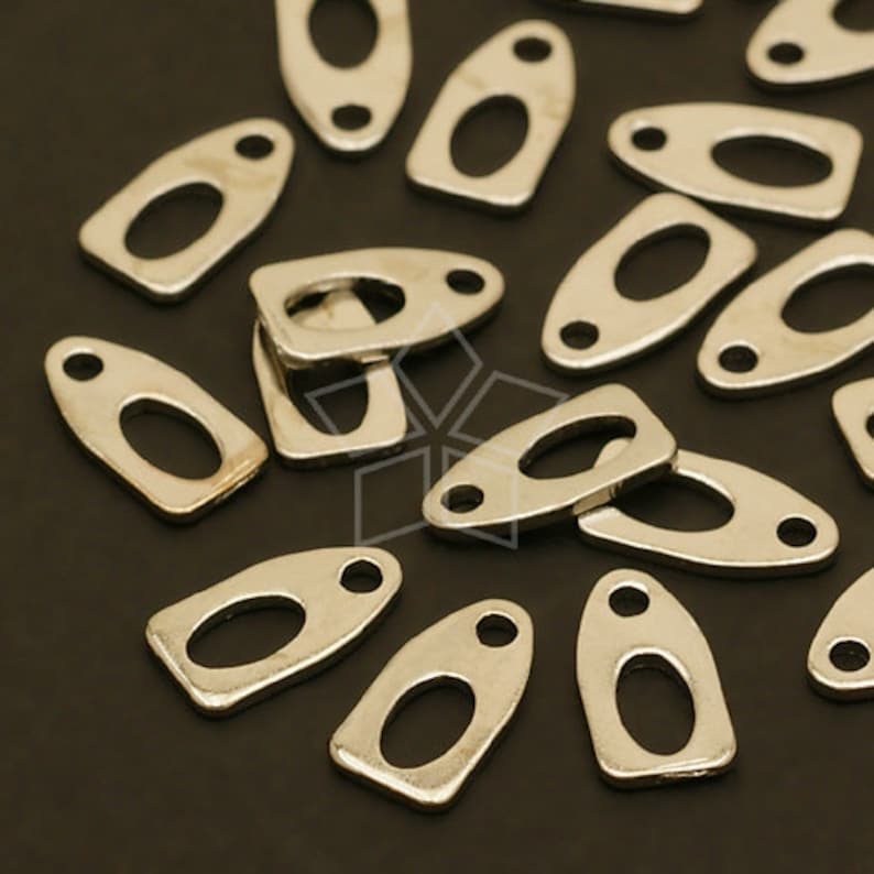 May include: A group of silver-toned metal oval-shaped charms with two holes each. The charms are scattered on a black surface.