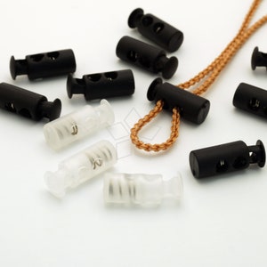 Puede incluir: Surtido de cierres de cordón de plástico negro y transparente con un mecanismo de resorte. Los cierres de cordón se utilizan para ajustar la longitud de los cordones y las correas.