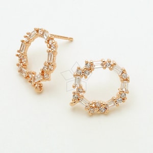 May include: A pair of gold-toned earrings with a circular design. The earrings are adorned with small, clear cubic zirconia stones.