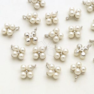 Puede incluir: Una colección de abalorios de metal plateado con un grupo de cinco cuentas de perlas blancas en forma de flor. Los abalorios tienen un bucle en la parte superior para sujetarlos a joyas u otras manualidades.