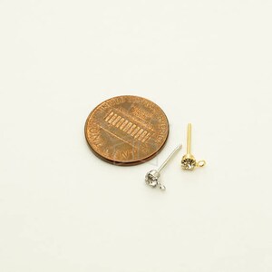 May include: Two silver earring posts with clear rhinestones, next to a US penny for size comparison.