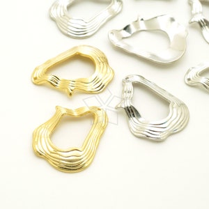May include: A set of gold and silver metal charms shaped like a wavy, abstract, organic form with a hole in the center. The charms are perfect for jewelry making or crafting.
