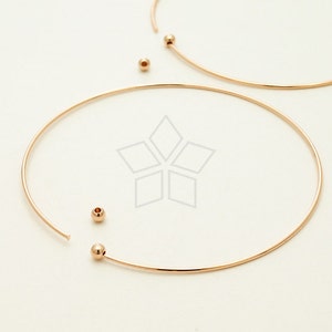 May include: A gold-toned choker necklace with two small round beads. The necklace is made of thin wire and is open at the back.