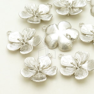 Puede incluir: Una colección de abalorios de flores de metal plateado con un acabado texturizado. Los abalorios tienen un diseño de flor de cinco pétalos con un pequeño bucle en la parte superior para sujetarlos a joyas u otras manualidades.